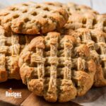 A close-up of freshly baked peanut butter cookies with a crisscross pattern on a wooden board.